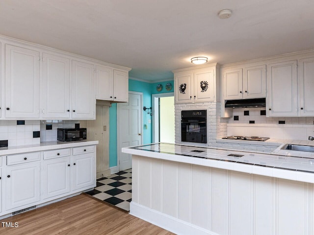 kitchen featuring oven, white cabinets, light floors, under cabinet range hood, and tile countertops