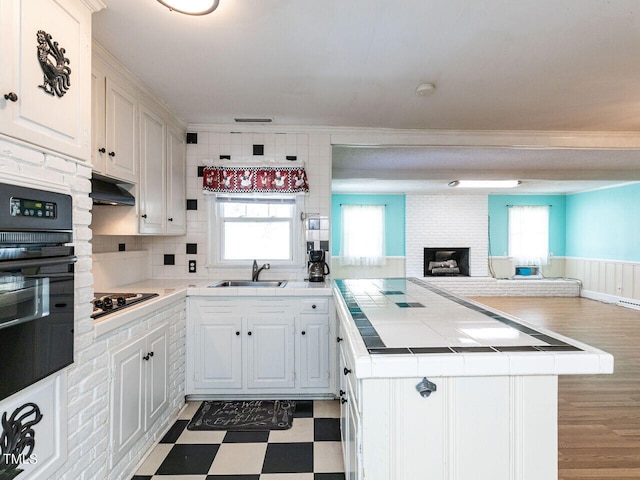 kitchen with tile countertops, a sink, tile patterned floors, a peninsula, and black appliances