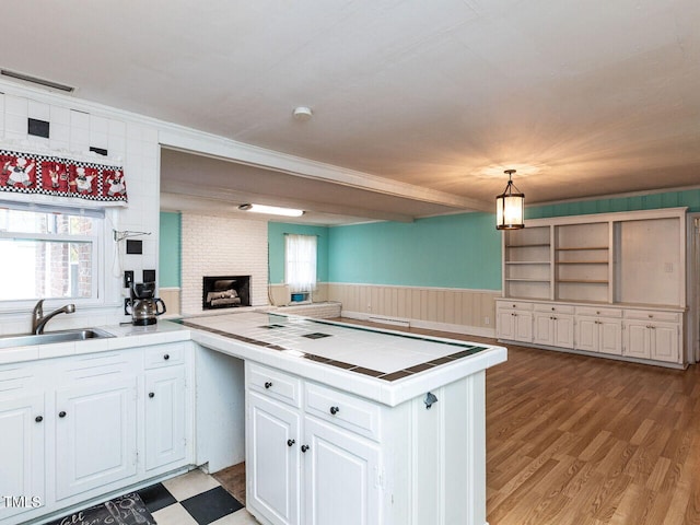 kitchen with a peninsula, a sink, a fireplace, tile counters, and white cabinets