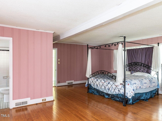 bedroom featuring ornamental molding, visible vents, a textured ceiling, and wood finished floors