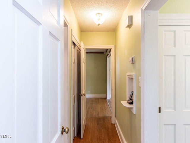 hallway featuring dark wood finished floors, baseboards, and a textured ceiling