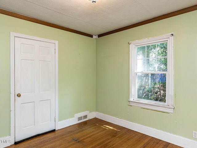 spare room with crown molding, visible vents, wood finished floors, and baseboards