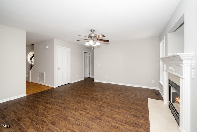unfurnished living room with ceiling fan, a premium fireplace, wood finished floors, and baseboards