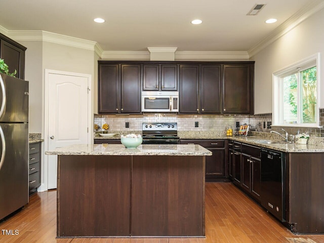 kitchen with stainless steel appliances, dark wood finished floors, dark brown cabinetry, light stone countertops, and ornamental molding