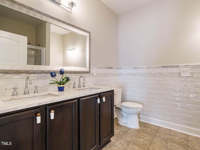 bathroom with double vanity, toilet, a wainscoted wall, tile walls, and tile patterned flooring