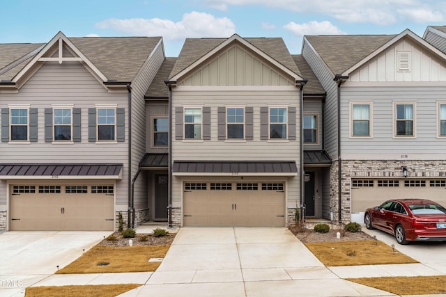 townhome / multi-family property featuring stone siding, driveway, a garage, board and batten siding, and a standing seam roof