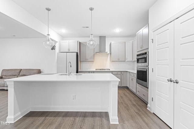 kitchen with gray cabinetry, open floor plan, wall chimney range hood, light wood-style floors, and stainless steel appliances