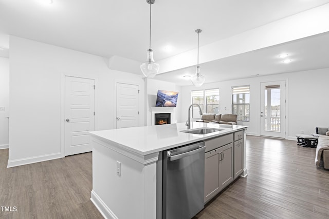 kitchen with a sink, open floor plan, stainless steel dishwasher, gray cabinetry, and a warm lit fireplace