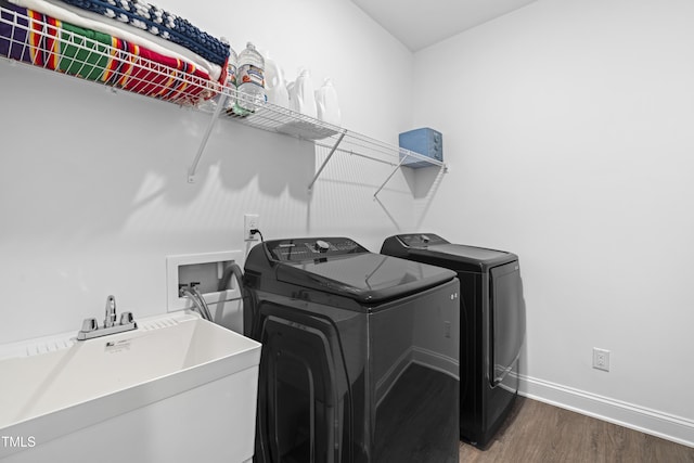 washroom with baseboards, washer and dryer, a sink, wood finished floors, and laundry area