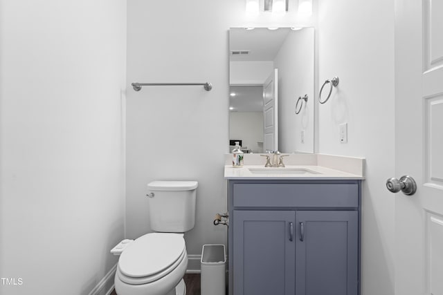 half bathroom featuring toilet, baseboards, vanity, and visible vents