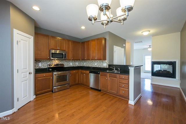8016 Sycamore Hill Ln, Raleigh, NC 27612 - kitchen featuring brown cabinets, wood finished floors, dark countertops, stainless steel appliances, and decorative backsplash