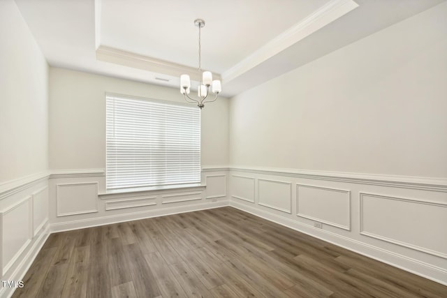 unfurnished room with a chandelier, a tray ceiling, ornamental molding, dark wood-style flooring, and a decorative wall