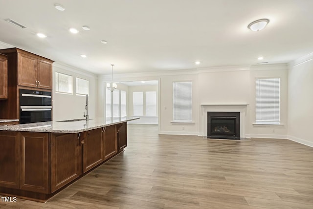 kitchen with ornamental molding, a sink, double wall oven, light stone countertops, and baseboards