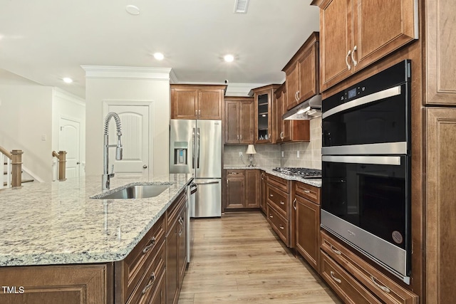 kitchen featuring stainless steel appliances, a sink, under cabinet range hood, ornamental molding, and light wood-style floors