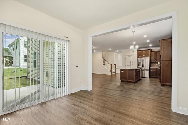 unfurnished living room with baseboards, a sink, a chandelier, dark wood-style flooring, and recessed lighting