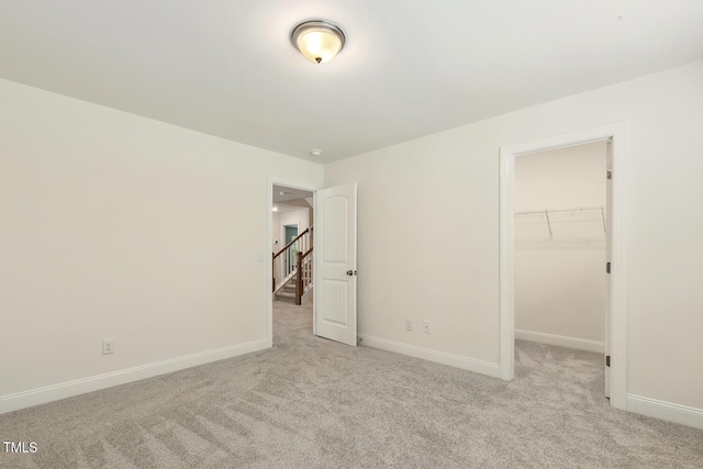 unfurnished bedroom featuring light carpet, baseboards, a spacious closet, and a closet