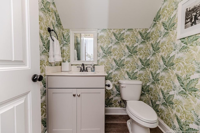 half bathroom with toilet, baseboards, vanity, and wallpapered walls