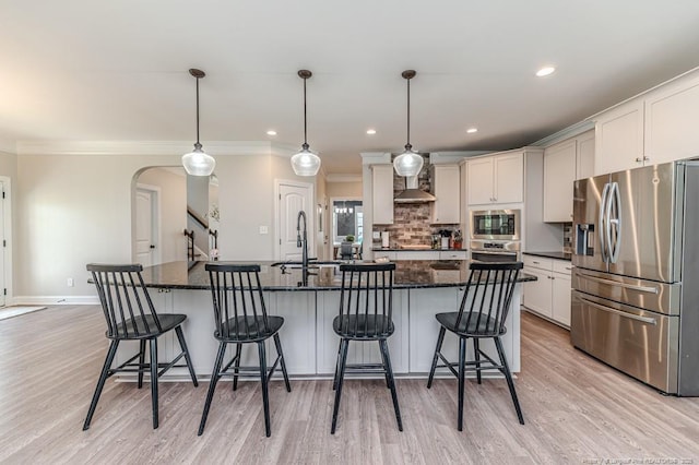 kitchen featuring a breakfast bar area, a sink, appliances with stainless steel finishes, arched walkways, and light wood-style floors