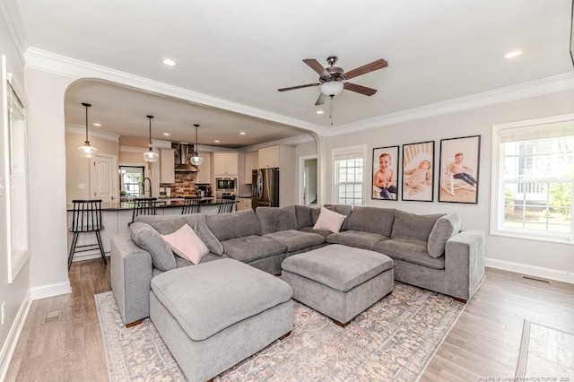 living room with ornamental molding, baseboards, a ceiling fan, and light wood-style floors