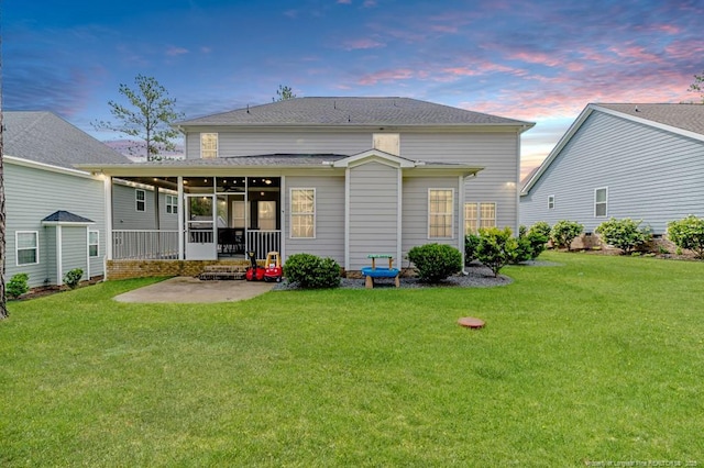 back of property at dusk with a lawn, a patio, a sunroom, and a shingled roof