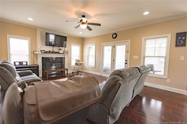 living area featuring a ceiling fan, baseboards, a glass covered fireplace, and crown molding