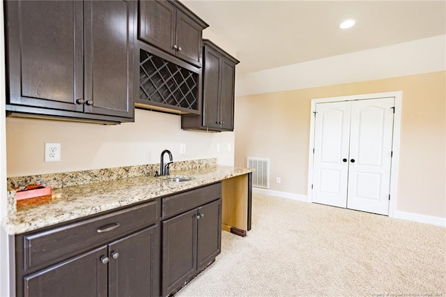 kitchen featuring a sink, light stone counters, dark brown cabinetry, light carpet, and baseboards