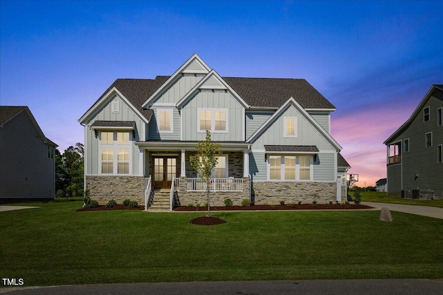 craftsman-style home with board and batten siding, covered porch, stone siding, and a front lawn