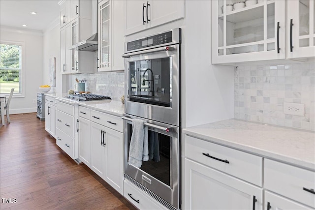 kitchen featuring appliances with stainless steel finishes, ornamental molding, decorative backsplash, light stone counters, and glass insert cabinets