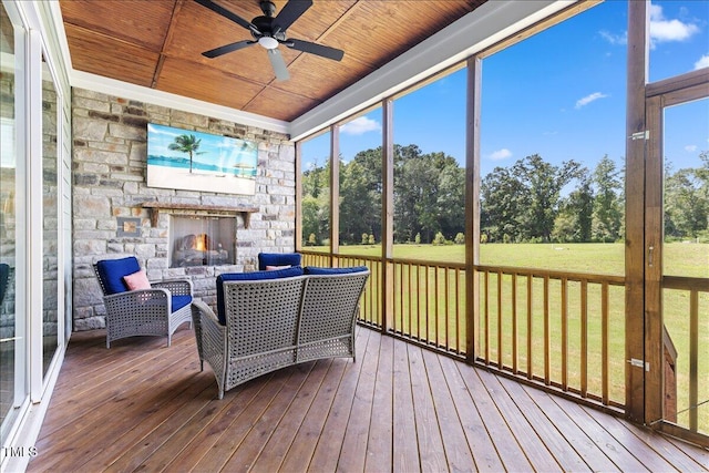 sunroom / solarium with a ceiling fan, an outdoor living space with a fireplace, and view of wooded area