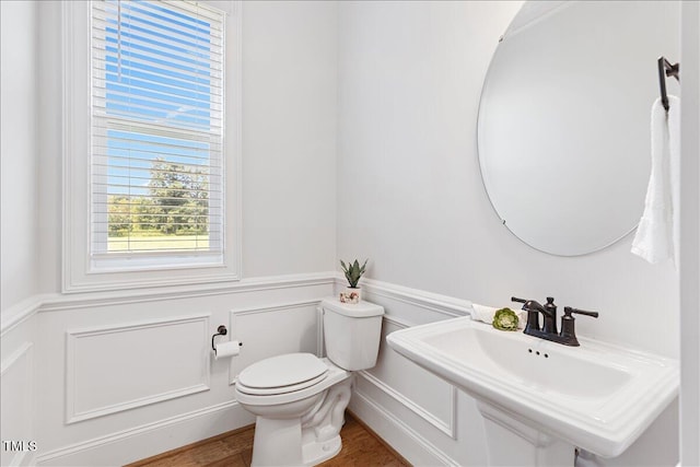 bathroom featuring a wainscoted wall, toilet, a sink, wood finished floors, and a decorative wall