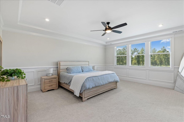 bedroom with a decorative wall, light colored carpet, wainscoting, ornamental molding, and a tray ceiling