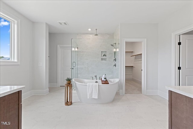 full bathroom with vanity, a shower stall, a soaking tub, a walk in closet, and baseboards
