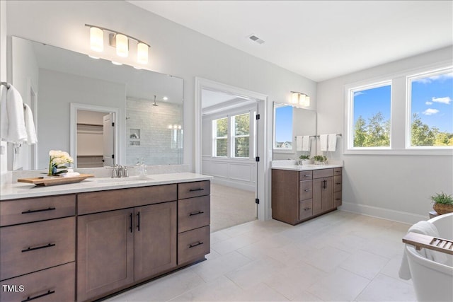 bathroom with plenty of natural light, tiled shower, two vanities, and baseboards