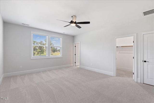 unfurnished bedroom with baseboards, light carpet, ceiling fan, and a walk in closet