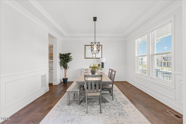 dining area with dark wood-style flooring, crown molding, wainscoting, and a decorative wall