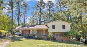 tri-level home featuring dirt driveway, a carport, and a front yard
