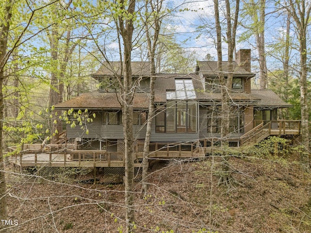 back of house with a chimney, roof with shingles, and a deck
