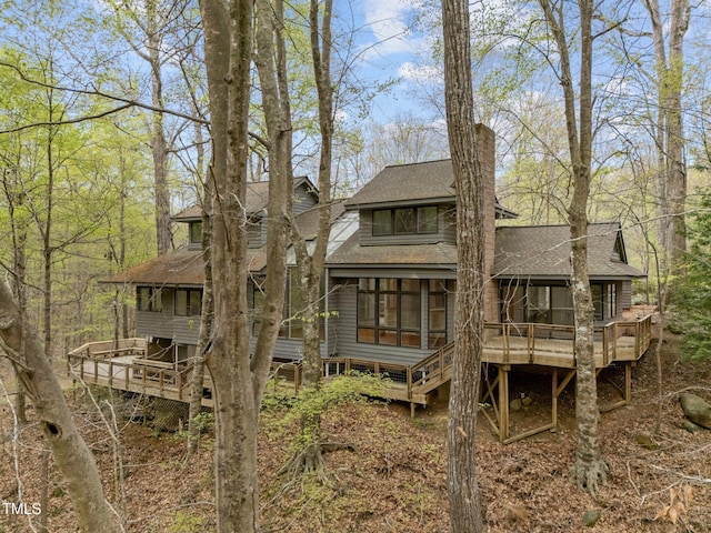 rear view of house featuring roof with shingles, a sunroom, a wooden deck, a chimney, and stairway