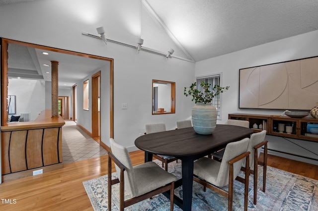 dining area featuring light wood-style floors, a textured ceiling, ornate columns, high vaulted ceiling, and baseboards