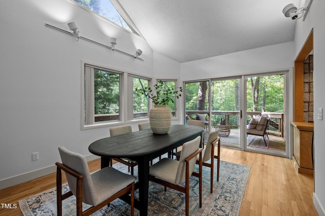 dining area with plenty of natural light, a textured ceiling, light wood-style flooring, high vaulted ceiling, and baseboards