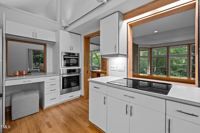 kitchen with stainless steel oven, black electric cooktop, light wood-type flooring, light countertops, and plenty of natural light