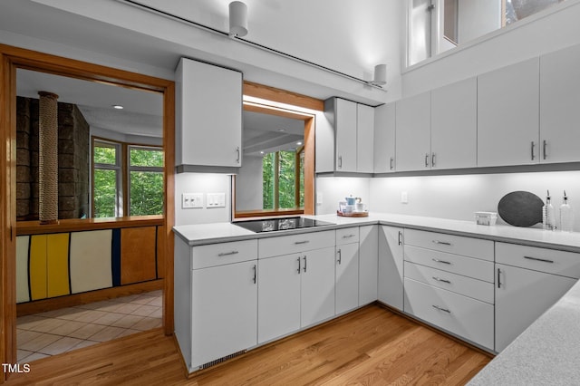 kitchen with black electric stovetop, light wood-style floors, and white cabinetry