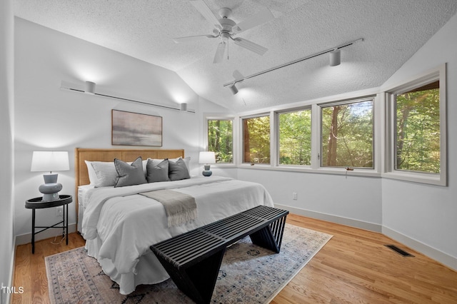 bedroom featuring a textured ceiling, baseboards, rail lighting, lofted ceiling, and wood finished floors