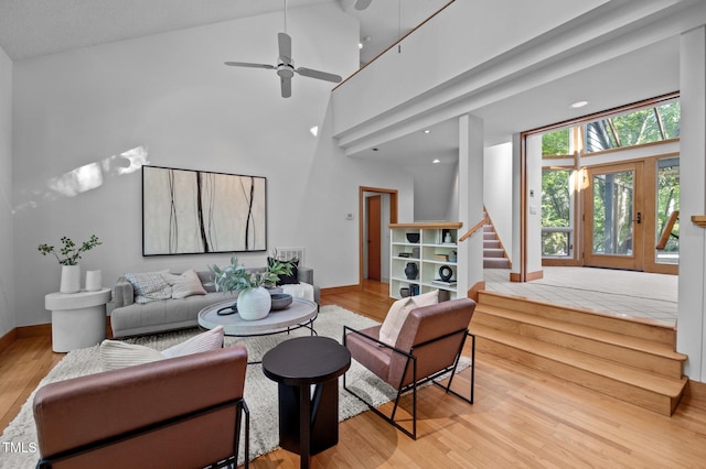 living area with stairs, wood finished floors, baseboards, high vaulted ceiling, and a ceiling fan