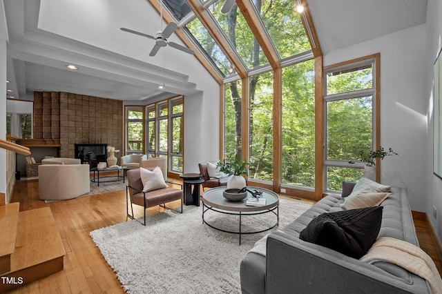 living area with a ceiling fan, a tile fireplace, vaulted ceiling, hardwood / wood-style flooring, and a sunroom