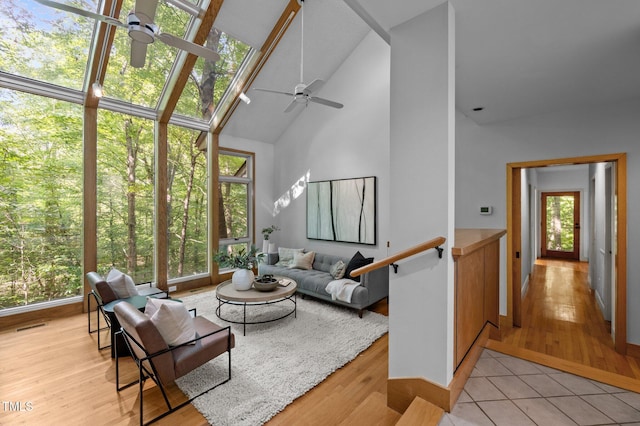 living room with a ceiling fan, high vaulted ceiling, light wood-type flooring, and baseboards