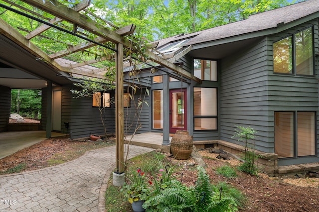 view of exterior entry featuring a pergola and roof with shingles