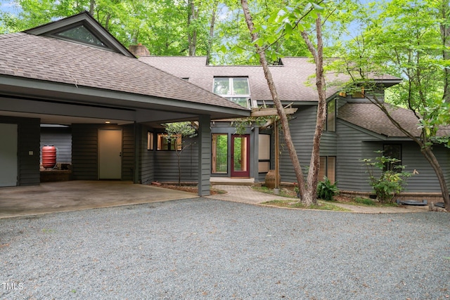 view of front of home with a shingled roof, a chimney, and gravel driveway