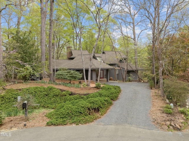 mid-century home featuring a chimney, a shingled roof, and driveway
