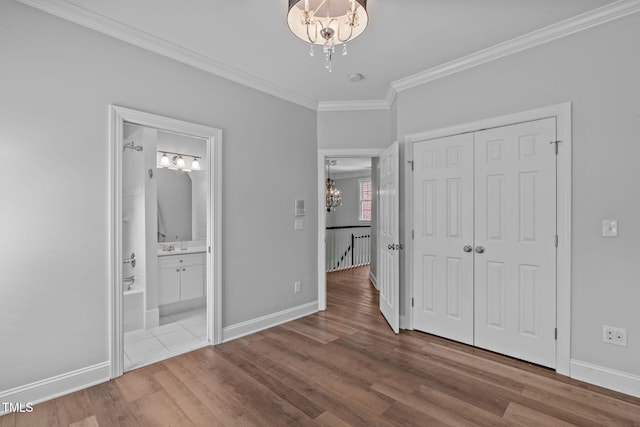 unfurnished bedroom featuring a chandelier, ornamental molding, wood finished floors, baseboards, and a closet